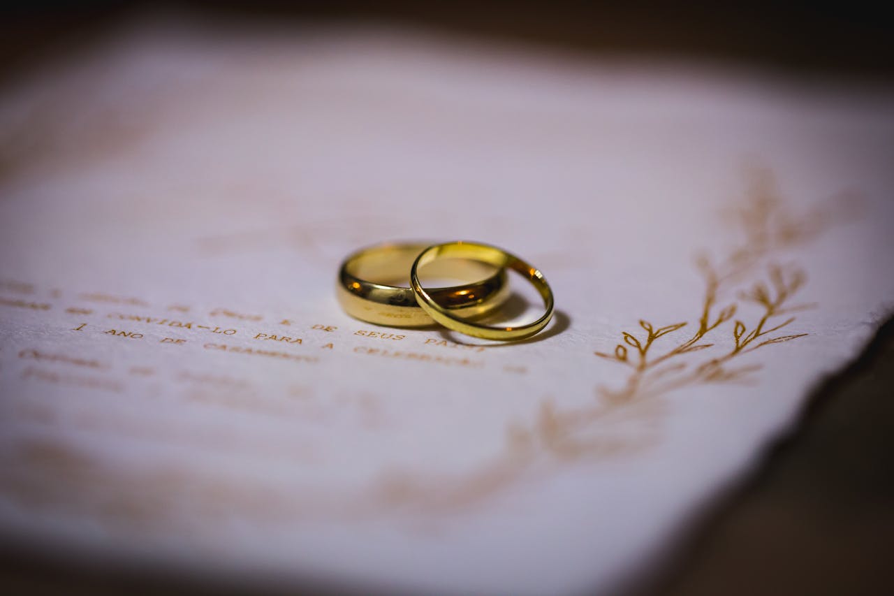 Two gold wedding rings resting on an elegant wedding invitation.