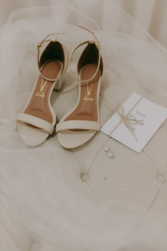 Elegant bridal shoes paired with an invitation and jewelry on soft lace fabric.
