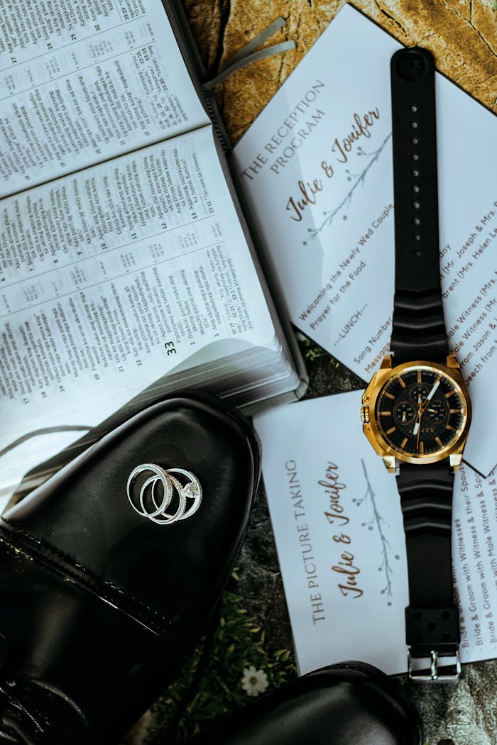Flat lay of wedding rings, invitation, shoes, and watch for a stylish groom.